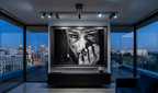 Modern living room with a large TV displaying a black and white image, overlooking a cityscape at night.