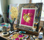 Artistic workspace with painting materials and a completed artwork on a wooden easel.